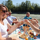 Zwei Frauen stoßen mit WUYD Whisky an, im Hintergrund Freunde beim Picknick an der Isar.