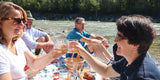 Zwei Frauen stoßen mit WUYD Whisky an, im Hintergrund Freunde beim Picknick an der Isar.