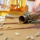 Copper Dipping Dog liegt auf Holztisch, Whisky tropft heraus. Daneben unscharf ein Glas mit Whisky.