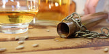 Copper Dipping Dog liegt auf Holztisch, Whisky tropft heraus. Daneben unscharf ein Glas mit Whisky.