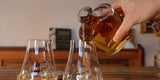 WUYD Whisky wird in zwei Nosinggläser eingeschenkt, die auf einem Holztisch stehen.