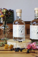 Kleine Flower Power Gin Flasche steht auf einer Holzscheibe.