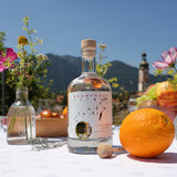 Eine Flasche Flower Power Gin auf einem sommerlich gedeckten Tisch mit Bergpanorama.