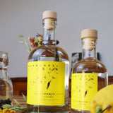 Eine große und eine kleine Flasche Flower Power Lemon Gin auf einem Tisch mit Dekoration.