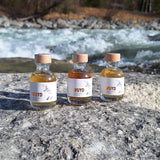 Drei kleine Flaschen mit WUYD Single Malt Whisky (Tasting-Set) stehen am Ufer auf einem Stein, im Hintergrund fließt die Isar.