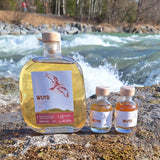 Eine große Flasche WUYD Single Malt Whisky Batch #3 steht neben zwei Miniaturflaschen mit Whisky am Ufer auf einem Stein, im Hintergrund fließt die Isar (WUYD Whisky Probier-Paket).