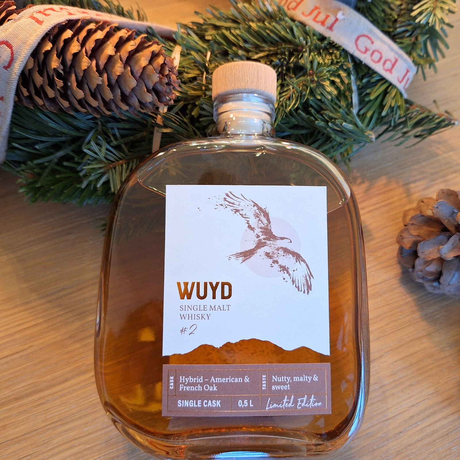 Eine Flasche WUYD Single Malt Whisky Batch 2 lehnt am Rand eines Adventskranzes.