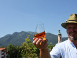 Ein Mann mit einem Hut hält vor Bergkulisse ein Nosingglas mit Whisky in seiner Hand.