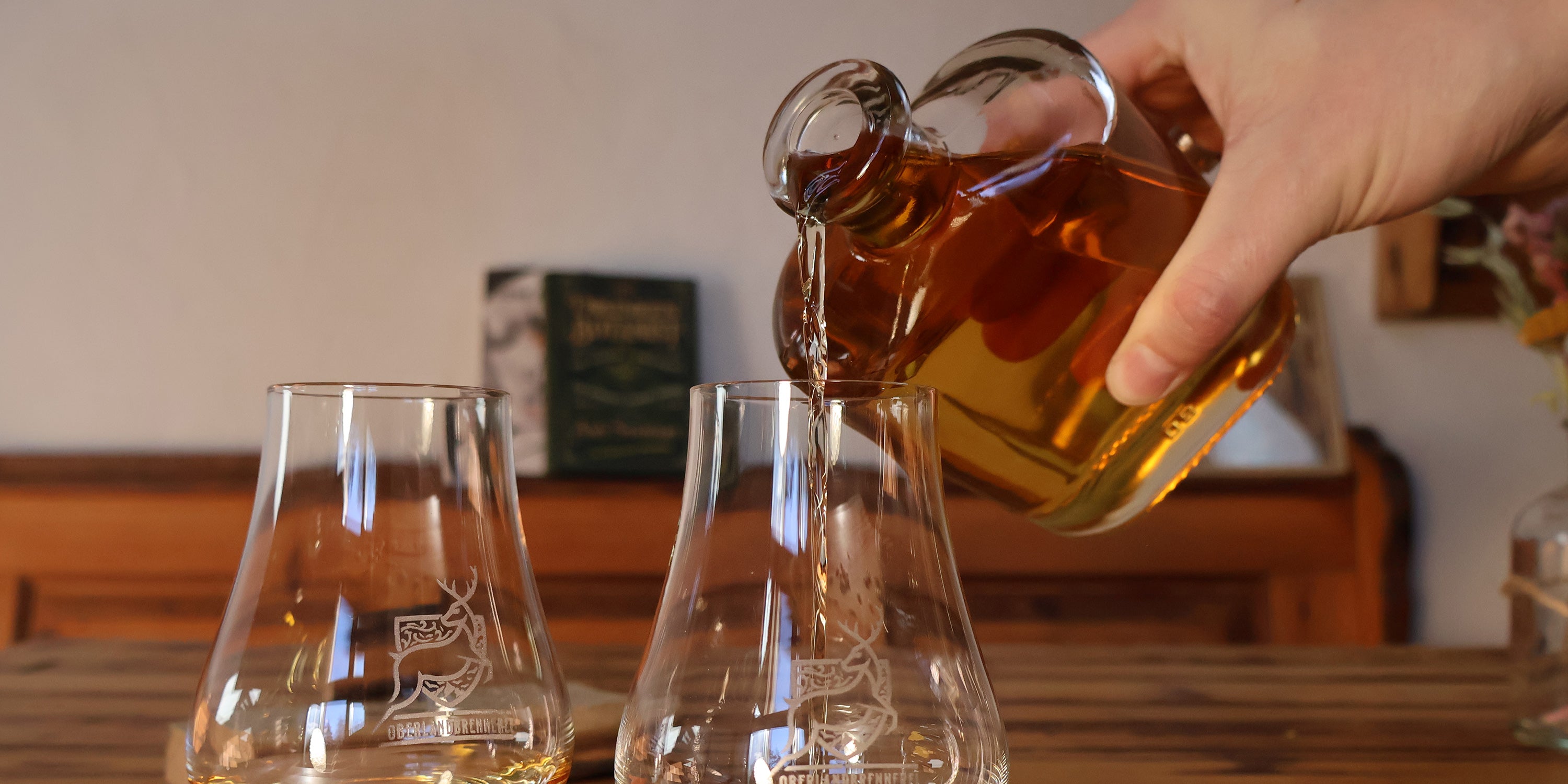 WUYD Whisky wird in zwei Nosinggläser eingeschenkt, die auf einem Holztisch stehen.