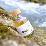 Eine Flasche WUYD Single Malt Whisky Batch #3,5 aus dem Hagebuttenweinfass liegt auf einem Stein, dahinter fließt die wilde Isar.