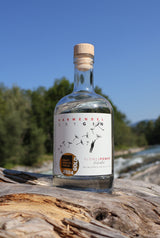 Eine Flasche Flower Power Gin steht auf einem Holzstamm, im Hintergrund fließt die Isar.